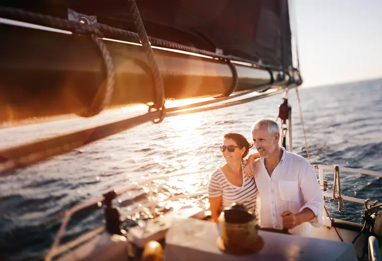 Coppia sorridente su una barca a vela al tramonto, rappresenta lo sviluppo del patrimonio.