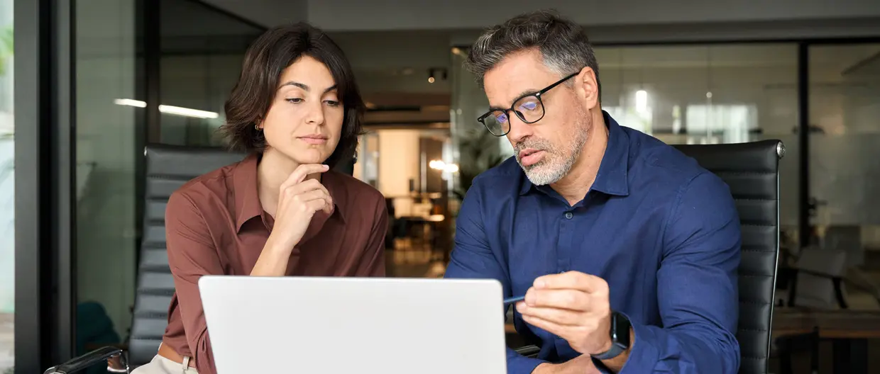Due colleghi, uomo e donna, seduti alla stessa scrivania in ufficio mentre esaminano le nuove linee guida ESMA sulla denominazione dei fondi visualizzate sul computer portatile aperto davanti a loro.