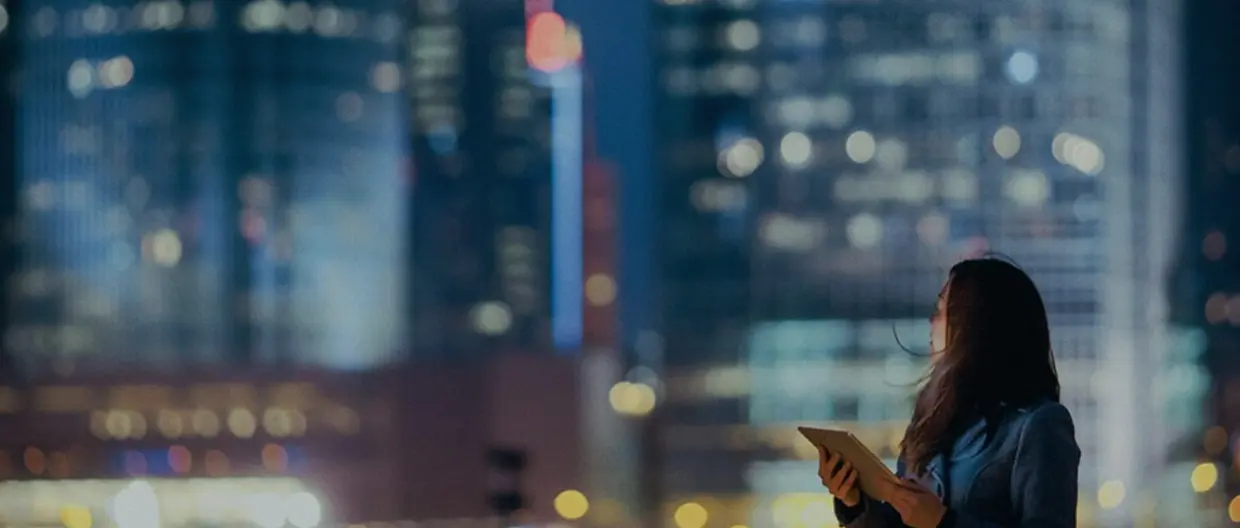 immagine di una ragazza con un tablet in mano su sfondo skyline notturno