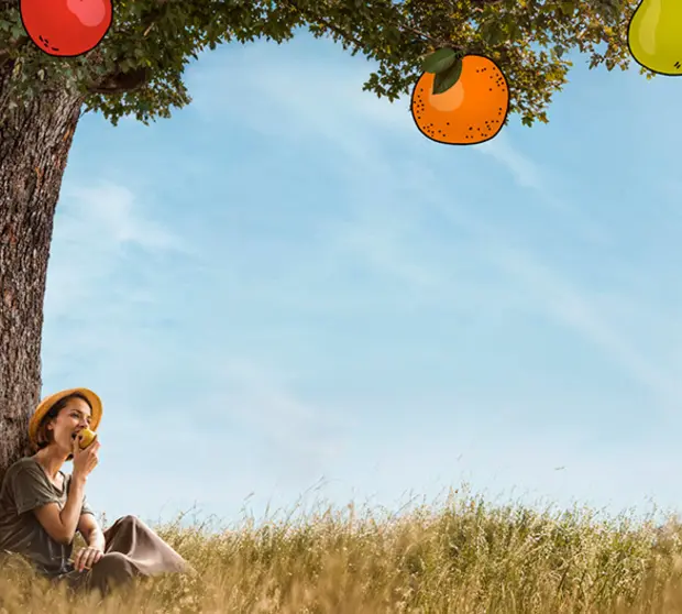 A woman eating an apple at the base of a fruit tree.