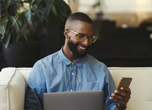 Man sitting on couch consulting phone and laptop