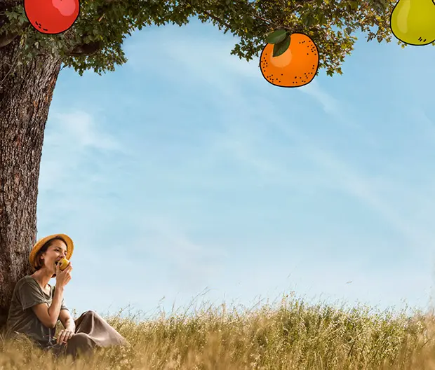 A woman eating an apple at the base of a fruit tree.