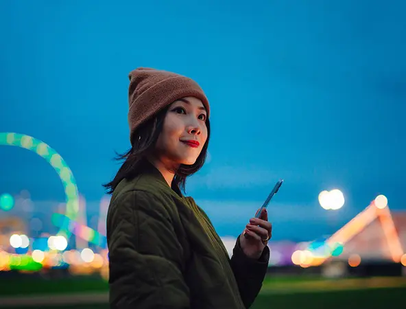 Sorridente giovane donna che utilizza uno smartphone in luna park